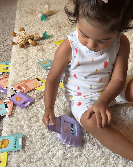 Szőnyegen ülő kislány a KinderSpeech beszédfejlesztő játékkal és a körülötte lévő oktatókártyákkal.